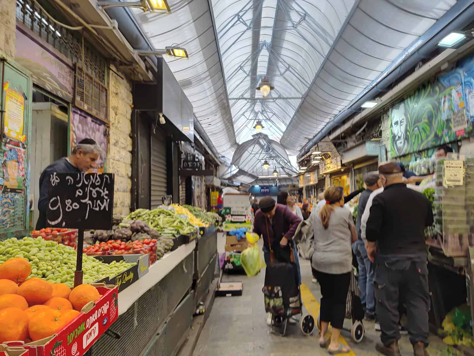 שוק מחנה יהודה בירושלים – לקוחות קונים ירקות ודוכנים עמוסים במחירים