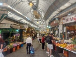 קונים ברחוב מקורה בירושלים בין דוכני ירקות, פרחים ומיצים