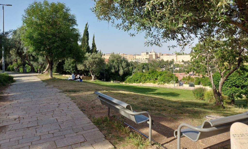 אנשים יושבים על הדשא במשכנות שאננים בירושלים ביום אביבי מול חומות העיר