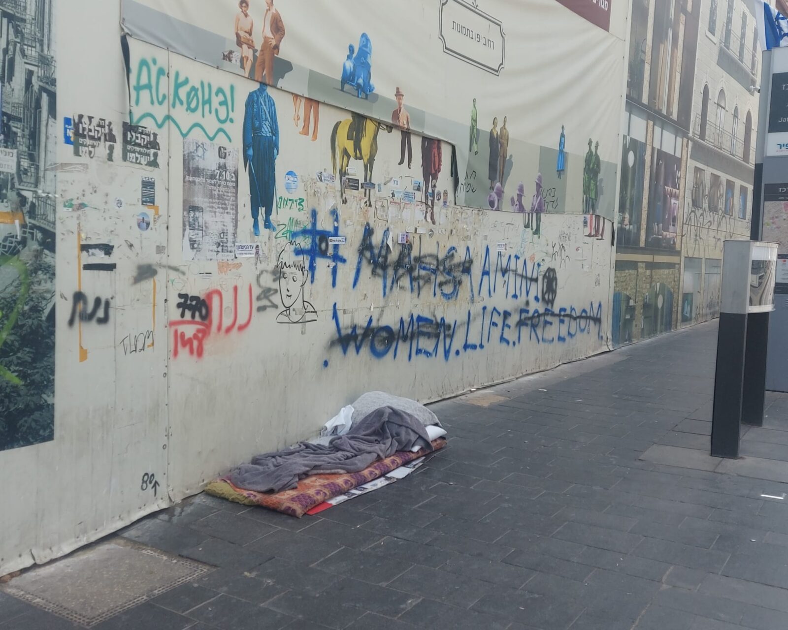 מראה של מקום לינה מאולתר (מזרן ושמיכות) על מדרכה בירושלים, המייצג את תופעת חסרי הבית והמצוקה ברחובות העיר.