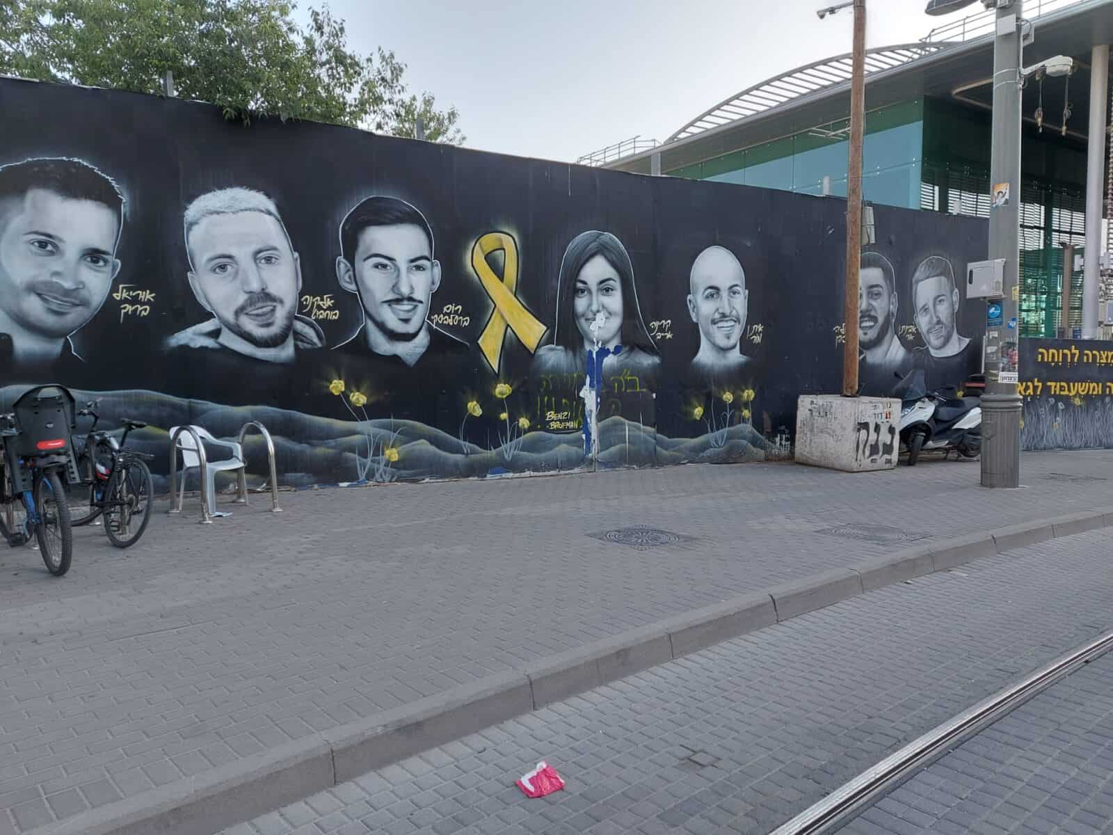 ציור קיר בירושלים ליד תחנת הרכבת נבון עם דיוקנאות חטופים, מראה סימני השחתה על דמות של חטופה ששבה. קשר להדרת נשים וזיכרון ציבורי