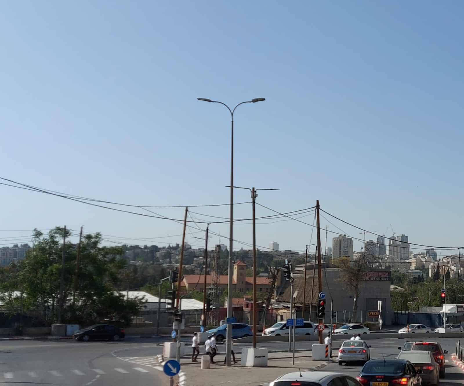 תמונת רחוב בירושלים עם תנועת מכוניות ואוטובוס, בניינים ברקע, ורמזור ירוק בבוקר בהיר