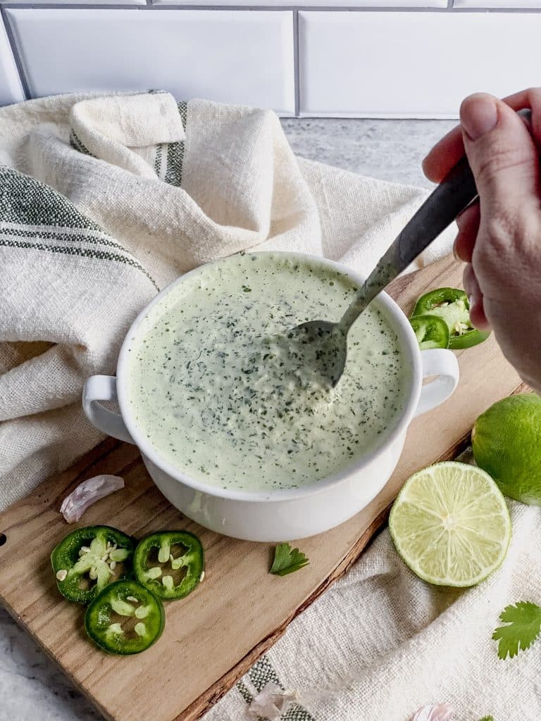 bowl of cilantro lime cream crema sauce with a spoon mixing it