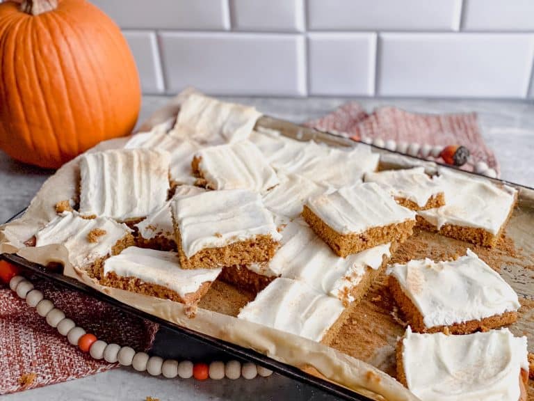 a pan of gluten free pumpkin bars with cream cheese frosting sits near an orange pumpkin in the background