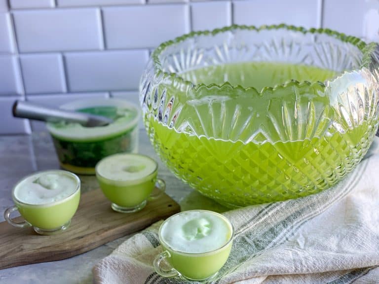 a bowl of green punch sits on counter with cups full of holiday punch and lime sherbet