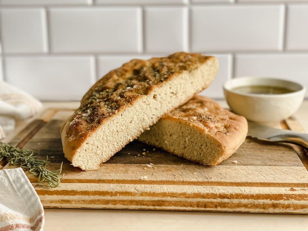 a sliced loaf of gluten free focaccia bread sits on a cutting board