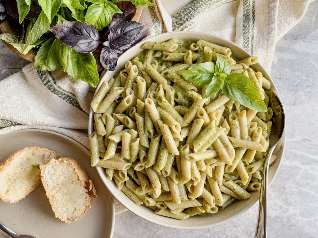 gluten free dairy free homemade basil pesto sauce on gluten free penne pasta noodles and a side of bread