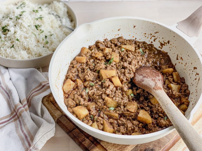 a white skillet filled with ground meat and potatoes for Mexican Picadillo and a wooden spoon