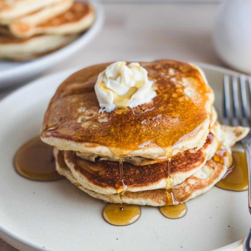 white plate with stack of homemade gluten free sourdough discard pancakes with syrup dripping off of them
