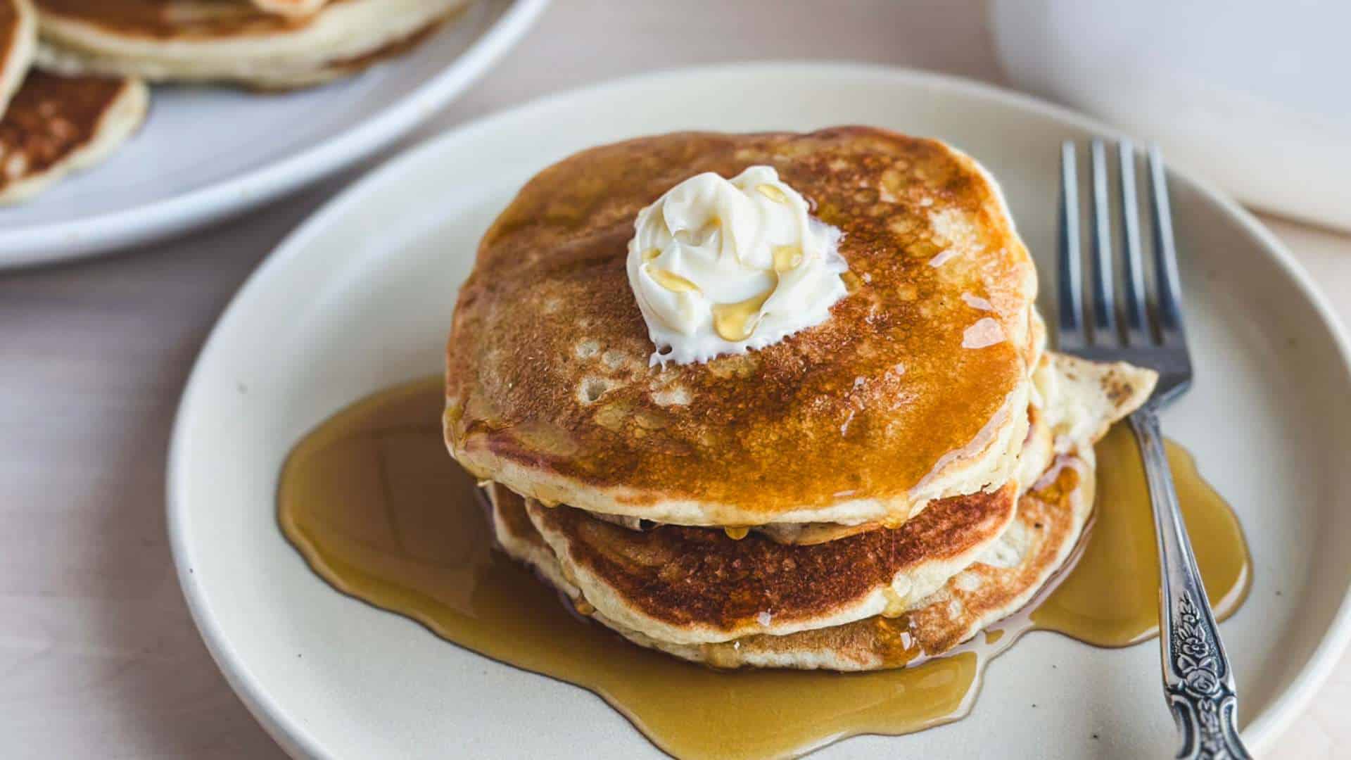 a tan plate holding a stack of gluten free sourdough pancakes with maple syrup and a fork nearby
