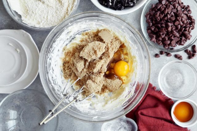 Brown sugar and an egg being added to creamed butter for cookies.