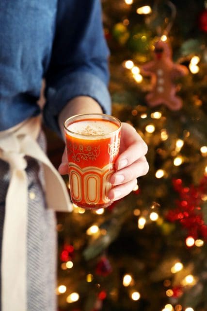 Hand holding eggnog at the Christmas tree.