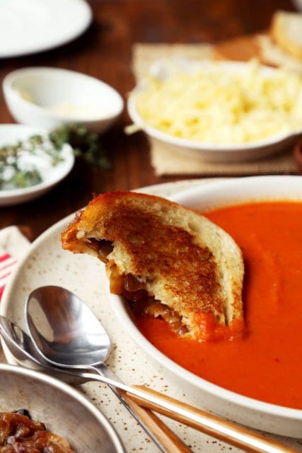 A grilled cheese sandwich dipped in tomato soup bowl.