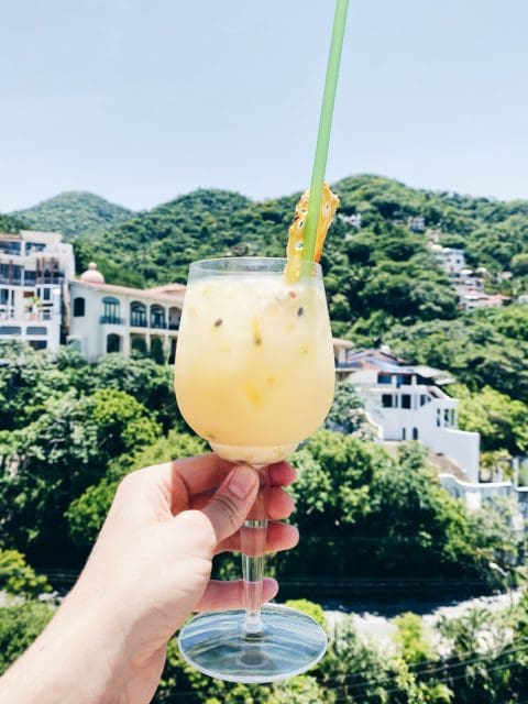 Full wine glass with straw held up against green mountains