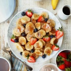 Platter of banana pancakes with sliced strawberries and fresh blueberries