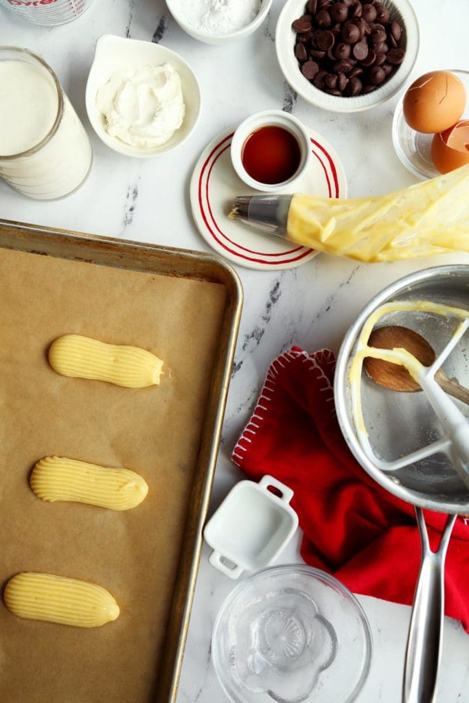 Eclair recipe batter piped onto parchment lined baking sheet