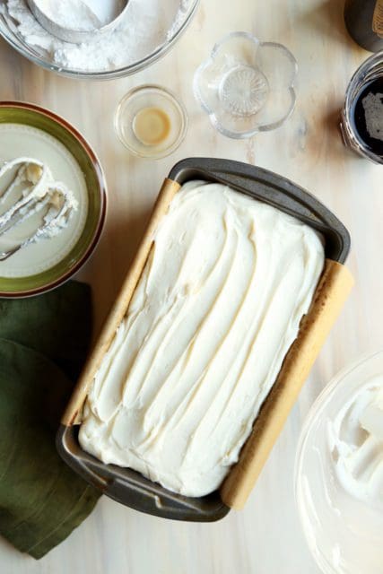 Cream cheese frosting spread over chocolate cake in a loaf plan.