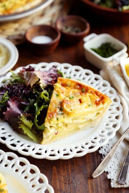 A slice of potato leek quiche on a white plate with salad.