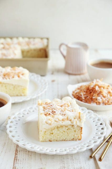 Slice of coconut cake on small white plate with coffee.