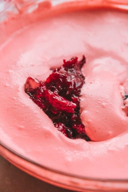 Adding cranberry sauce to pie filling in large clear bowl.