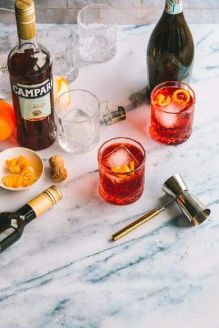 Two glasses of Negroni Sbagliato on a marble countertop.