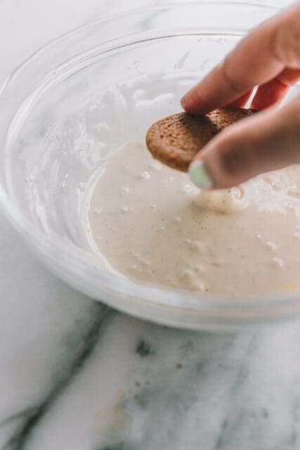Dipping baked oatmeal cookies in a bowl of glaze.