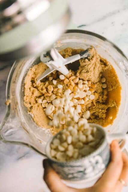 adding white chocolate chips to macadamia nut cookie batter in a stand mixing bowl