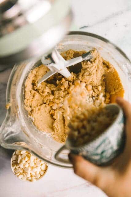 mixing toasted macadamia nuts into cookie batter in a stand mixing bowl