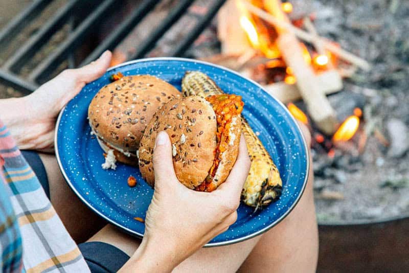 person holding a sloppy joe sandwich next to a campfire