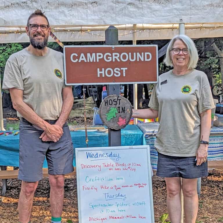 couple standing near a campground host sign