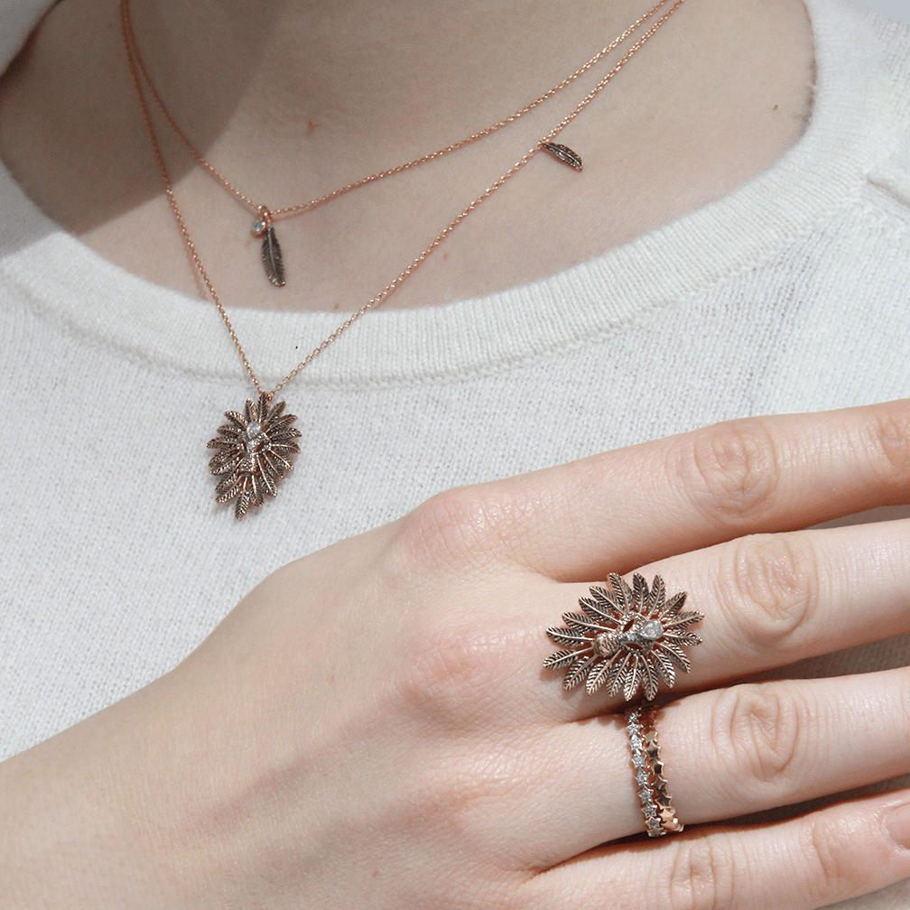 A person wearing a golden necklace showing their hand wearing two golden rings.