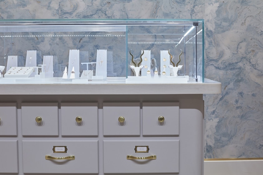 A glass display and several jewelry with a blue patterned wall behind.
