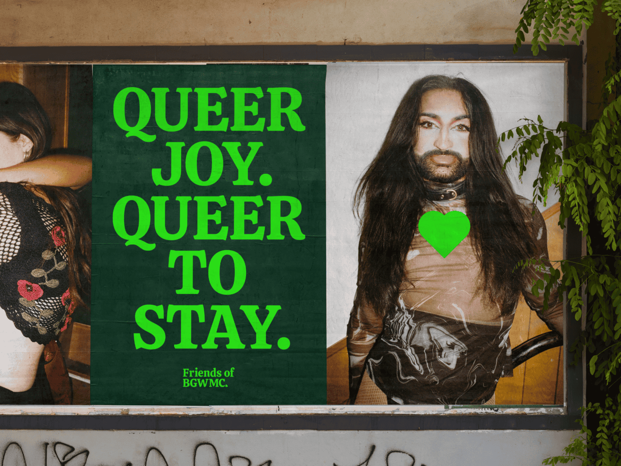 Poster on a wall at Bethnal Green with bold green text reading QUEER JOY. QUEER TO STAY. Next to it is an image of a person with long hair, a beard, wearing a patterned shirt and green heart necklace. Leaves partly frame the poster, capturing the lively essence of Friends Working Mens Club.