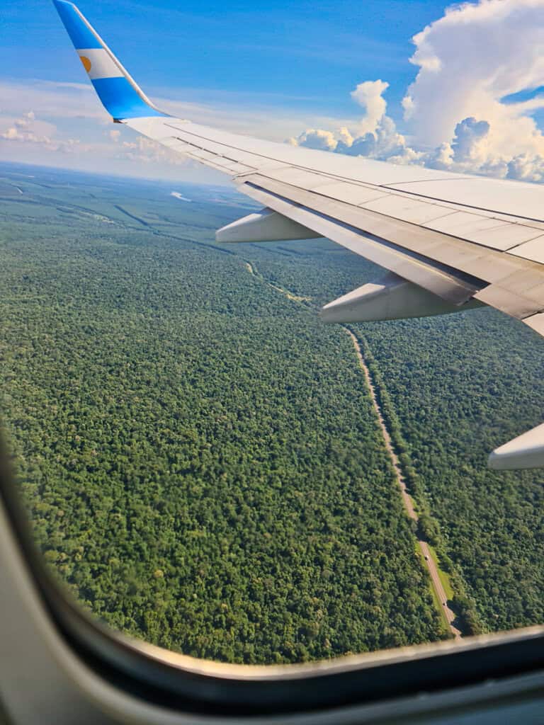 The view from an airplane window overlooking a dense, lush jungle canopy. The picture is taken while the plane from Buenos Aires approaches Iguazu Falls Airport.