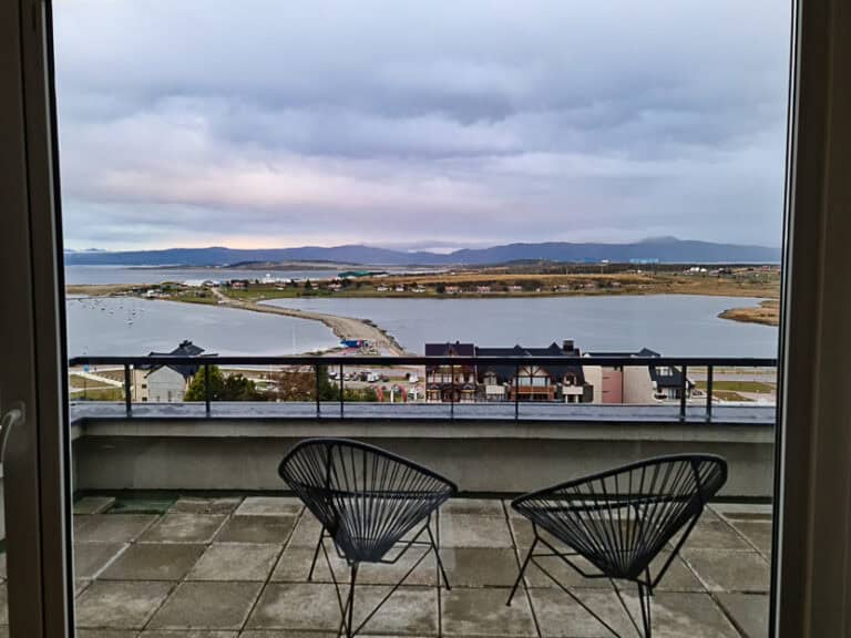 A serene view from a balcony at an Ushuaia accommodation, overlooking the bay, distant mountains, and shoreline. Ideal lodging choice for relaxing and enjoying Ushuaia’s natural beauty