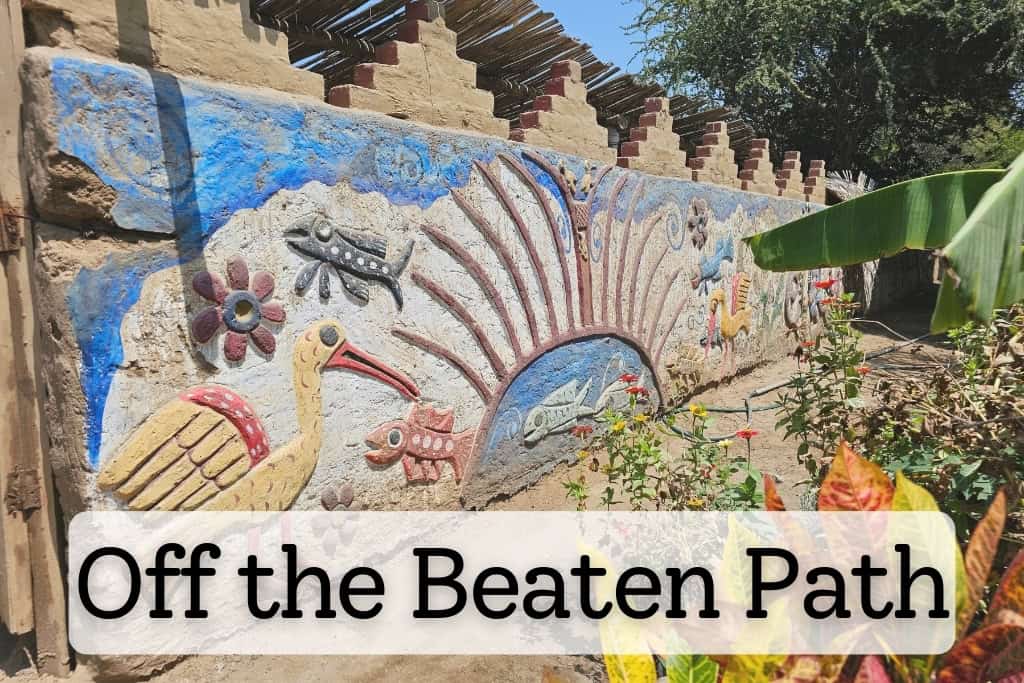 Vividly painted adobe wall with colorful, intricate designs of birds, fish, and flowers in a remote village setting, symbolizing off-the-beaten-path travel and cultural exploration.