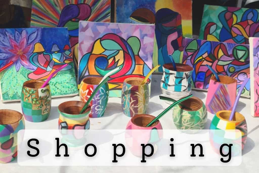 Colorful handcrafted items, including vibrant paintings and decorated wooden cups with straws, displayed at a local market, showcasing unique shopping opportunities and artisanal crafts.