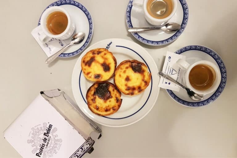 Golden Pastéis de Belém custard tarts served alongside espresso cups—an essential sweet treat in Lisbon’s food scene and a beloved Portuguese pastry.