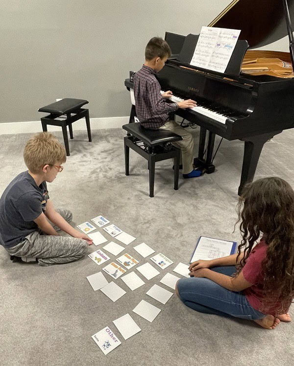 Student playing piano while two students organize cards on the floor