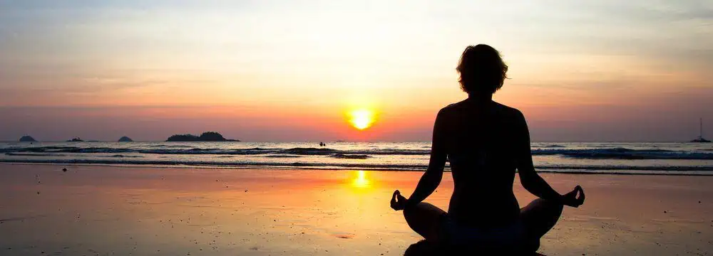 A man performing yoga positions on the beach at sunrise