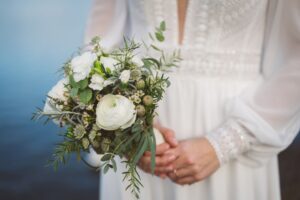 Detailaufnahme eines eleganten Brautstraußes mit weißen Blumen und grünen Akzenten, gehalten von einer Braut in Spitzenkleid – aufgenommen am Stadthafen Rostock.