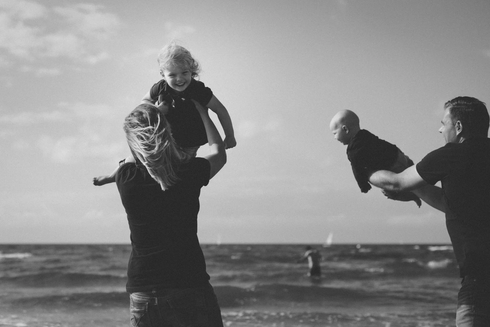 Familie am Strand von Warnemünde, Kinder werden in die Luft geworfen. Eine Familie am Strand von Warnemünde, die ihre Kinder spielerisch in die Luft wirft und lacht.