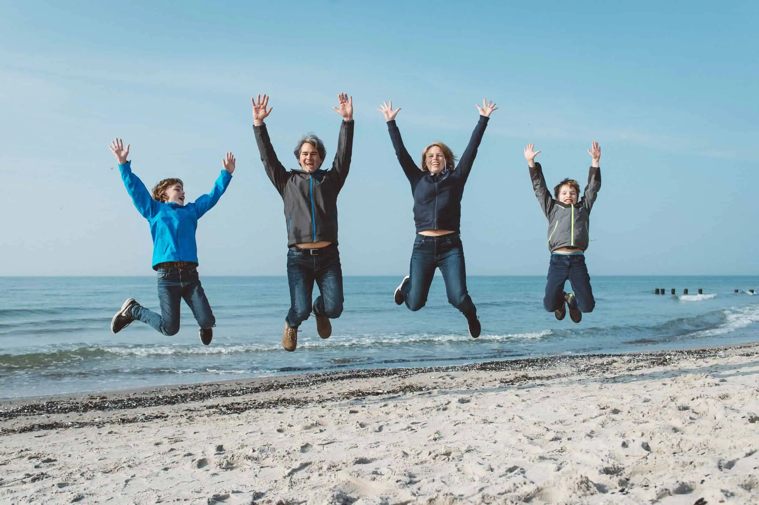 Der Familienshooting Gutschein vom Rostocker Fotograf macht Freude Fröhliche Familie hat ein Familienshooting Gutschein erworben und springt vor Freude am Ostseestrand in Rostock in die Luft