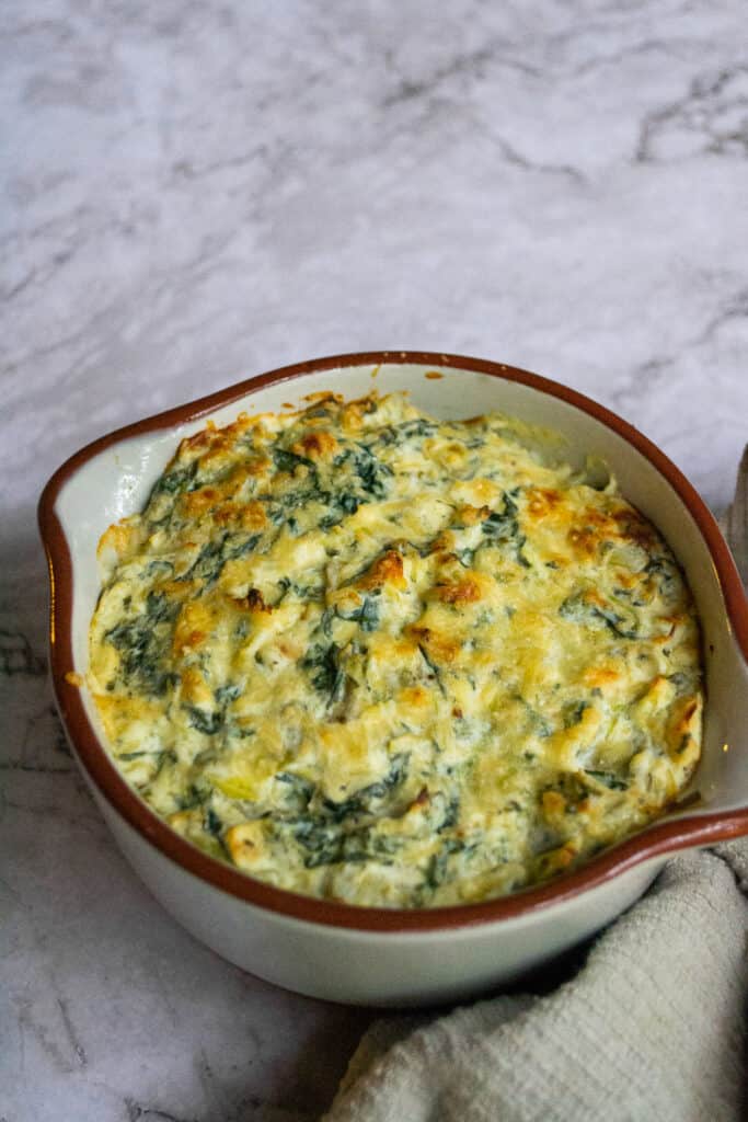 Healthy spinach artichoke dip in a bowl next to a cloth.