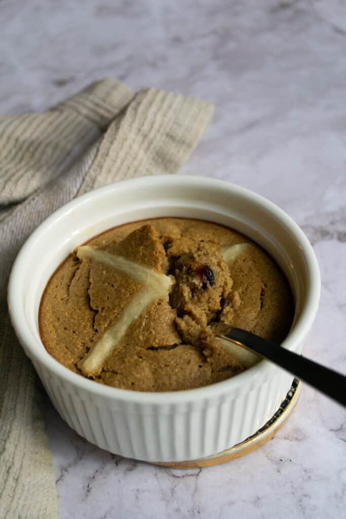 Hot cross bun baked oats with a bite taken out of it, with raisins visible inside.