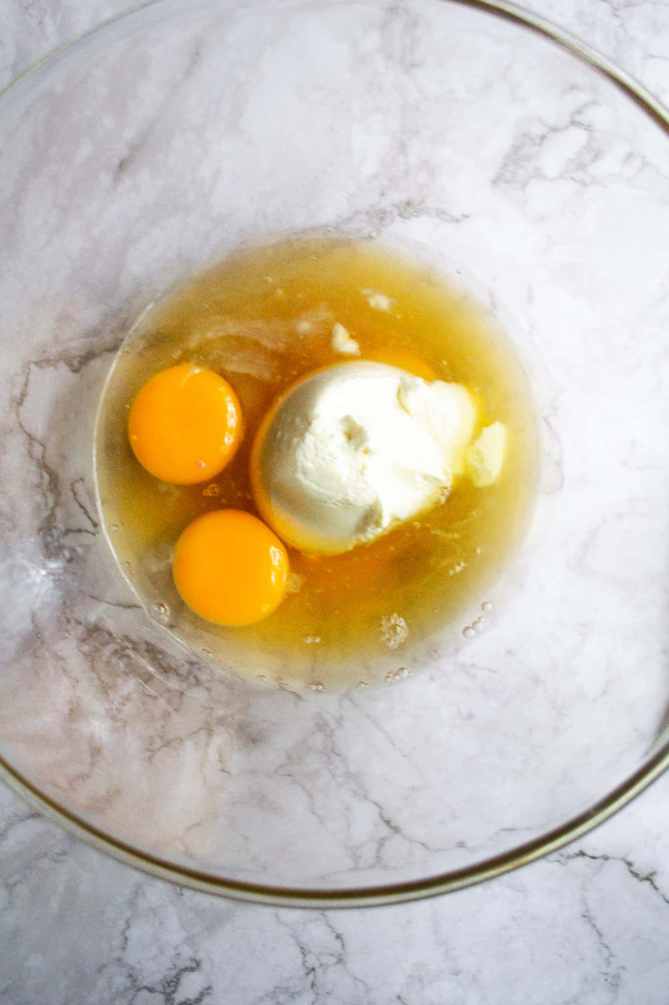 Loaf batter wet ingredients in a glass bowl. You can see honey, ricotta, eggs, and almond extract all in the bowl together unmixed.