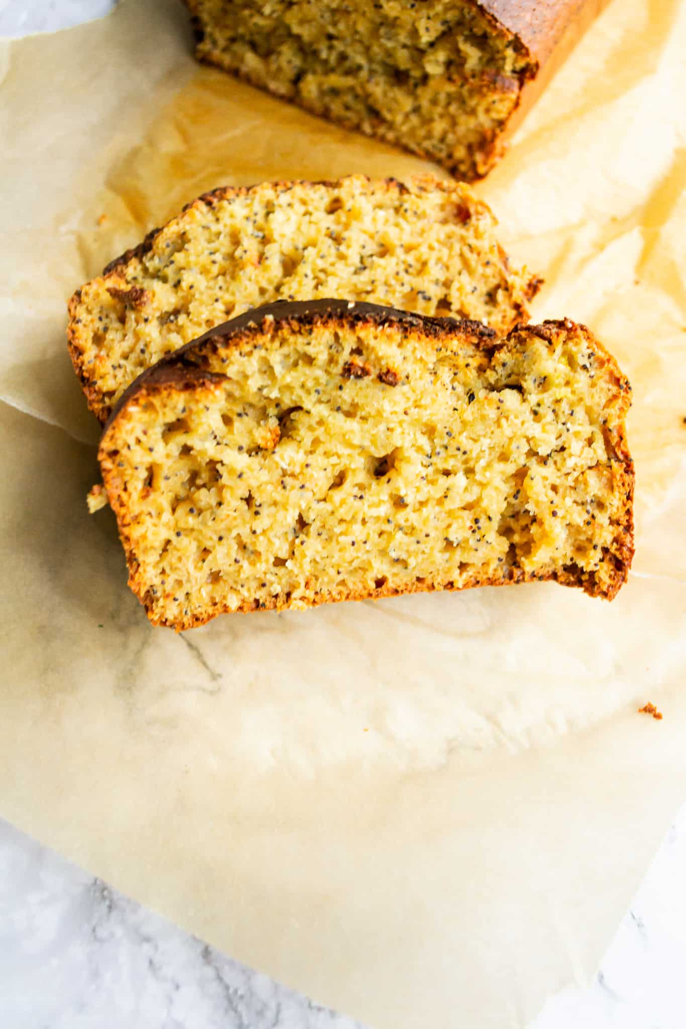 Two slices of orange poppyseed loaf on a piece of baking paper.