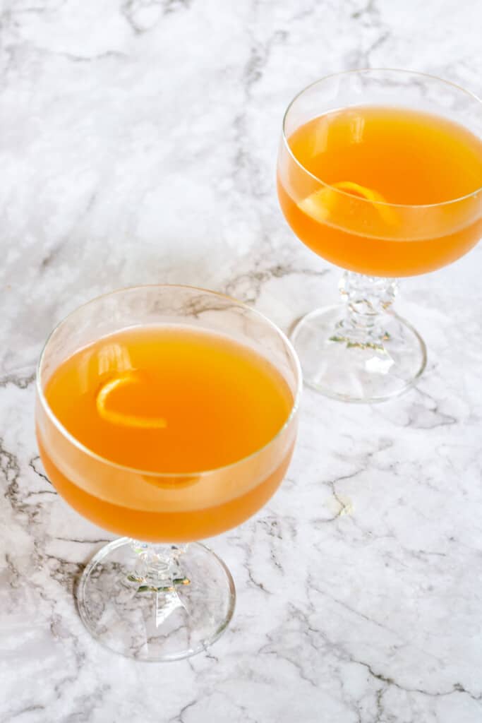 Two grapefruit daiquiris with a grapefruit twist on a marble table.