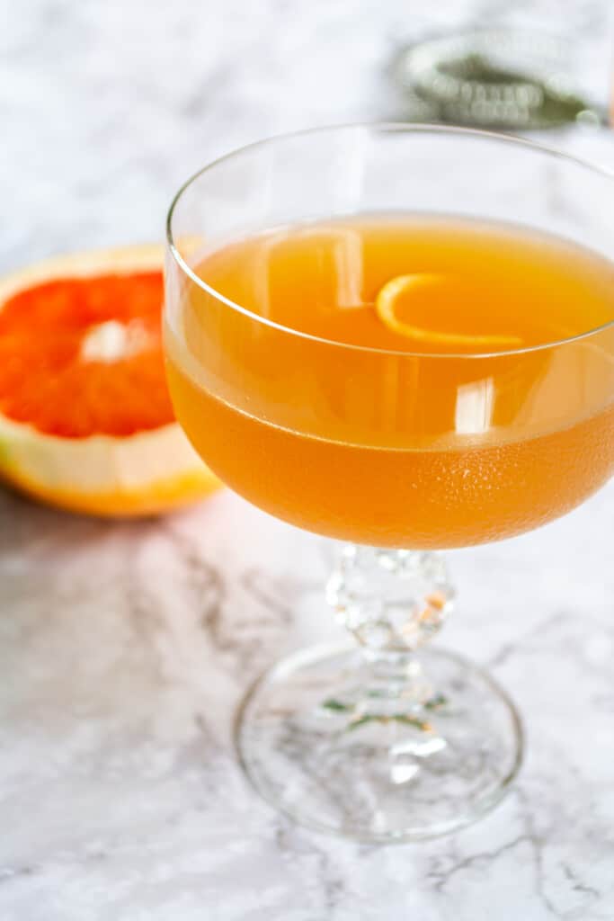 Grapefruit daiquiri in a crystal glass on a white marble table with a grapefruit in the background.