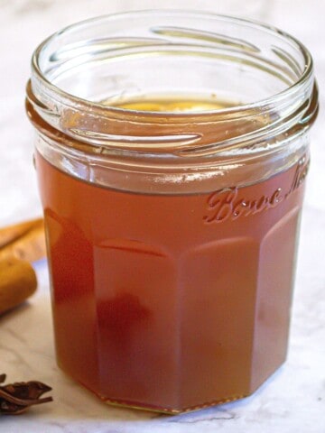 Fig simple syrup in a glass jar with spices including cinnamon and star anise in the background.